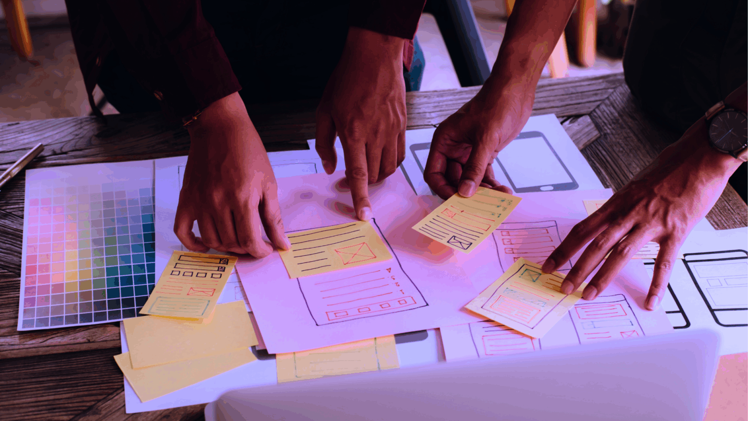 Hands of digital agency team members working on designs on a desk to prepare for a proposal.
