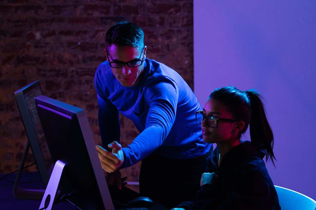 Two professionals collaborating at computer workstation with blue and purple lighting in modern office - accounting services for creative teams and collaborative businesses